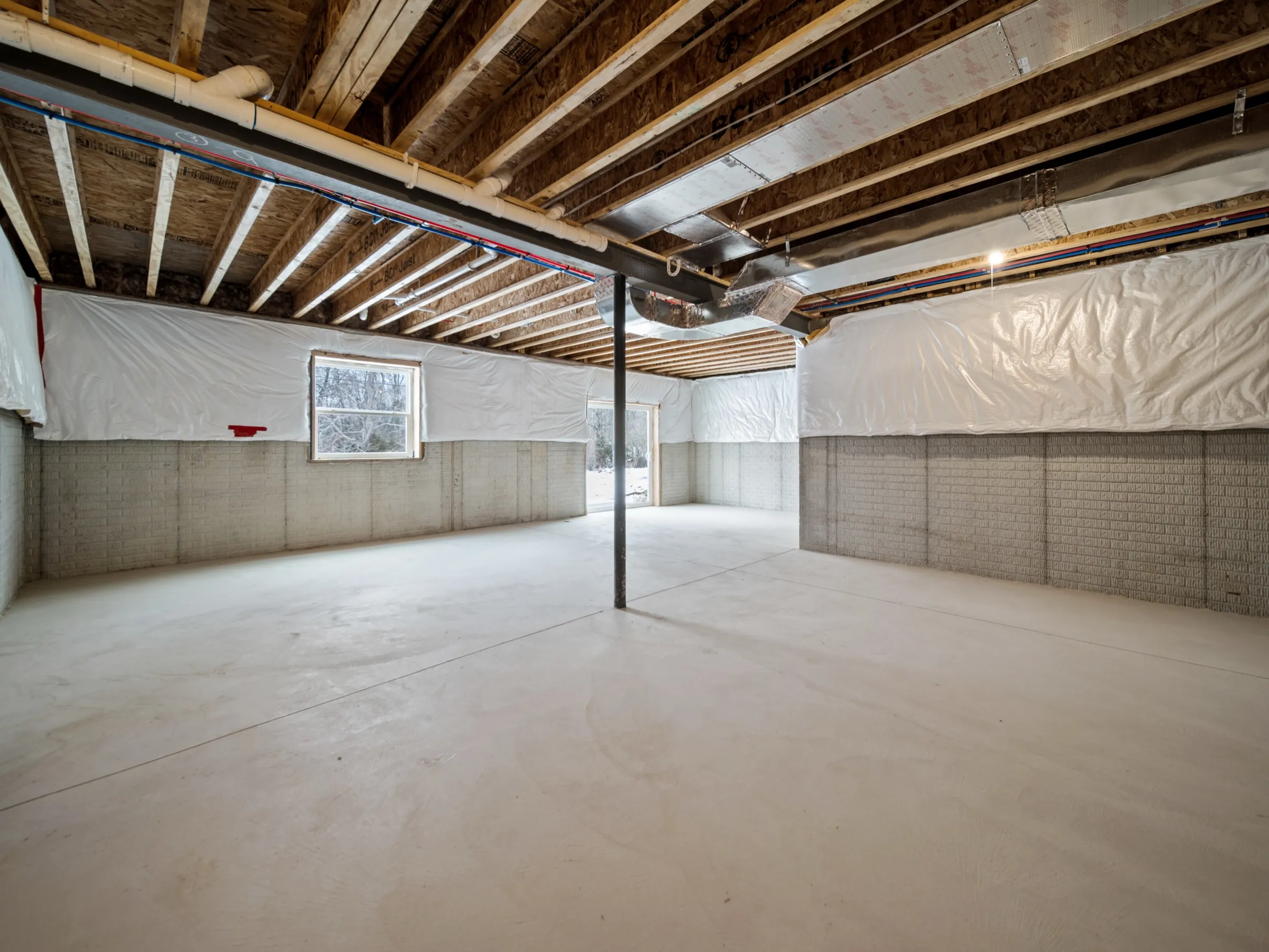 Unfinished full basement with a poured floor, steel beam, framed stair wall, and insulation wrapped along the walls.