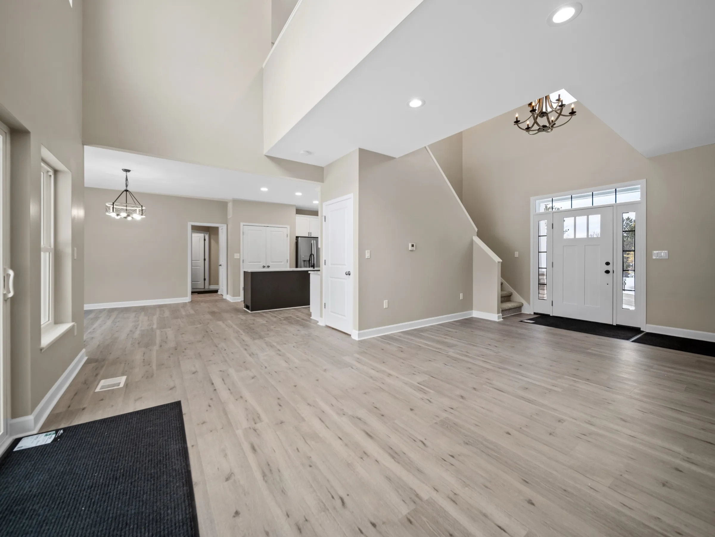 Open two-story foyer with the staircase rising over the front door, looking across new plank flooring to the kitchen.