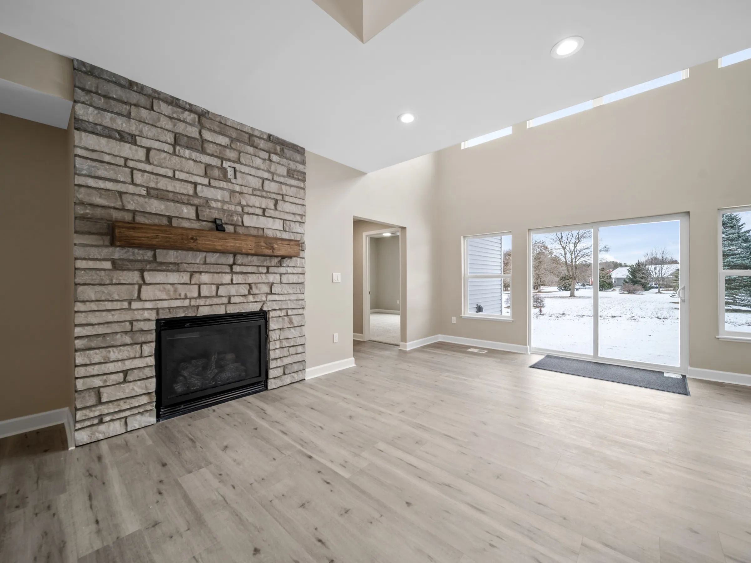 Living room with a floor-to-ceiling stone fireplace and timber mantel, a row of high windows, and a sliding door to the back yard.