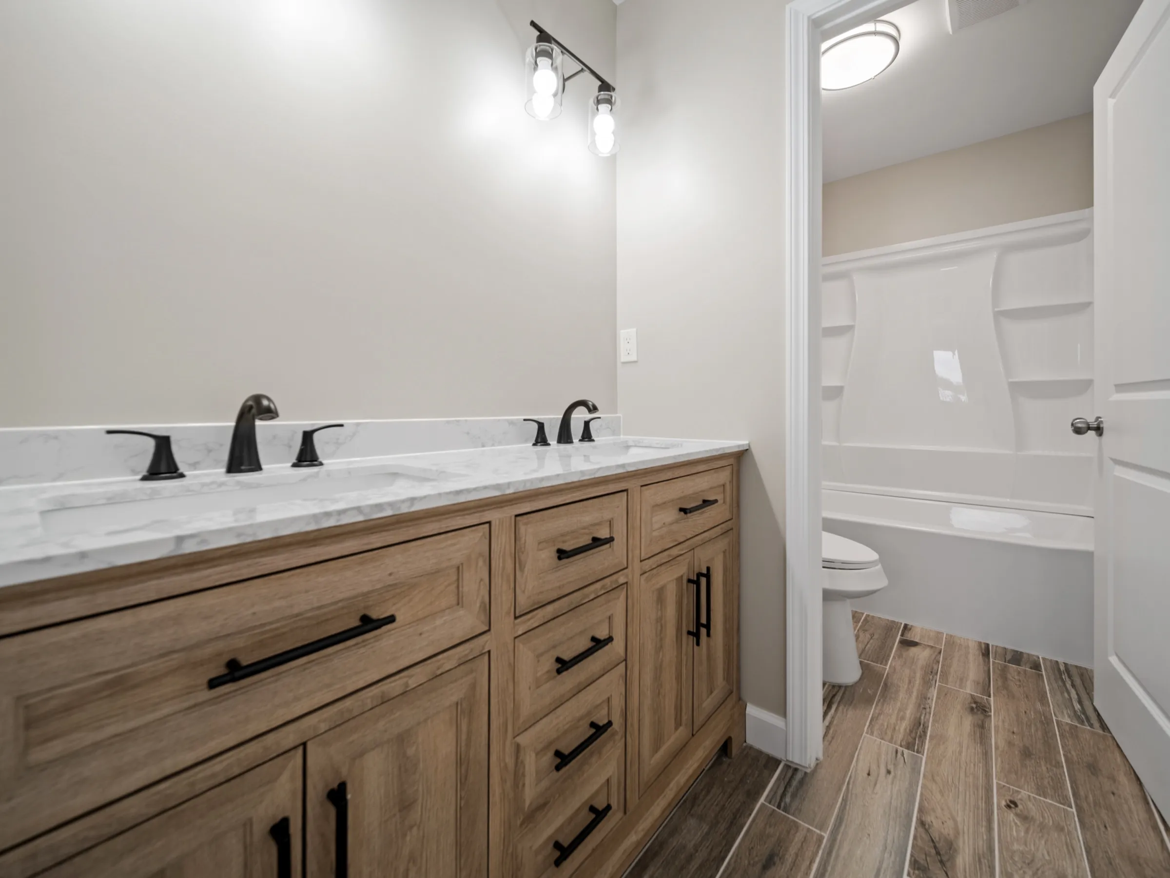 Bathroom with a double oak vanity and marble-look top, looking through to the tub and shower surround.