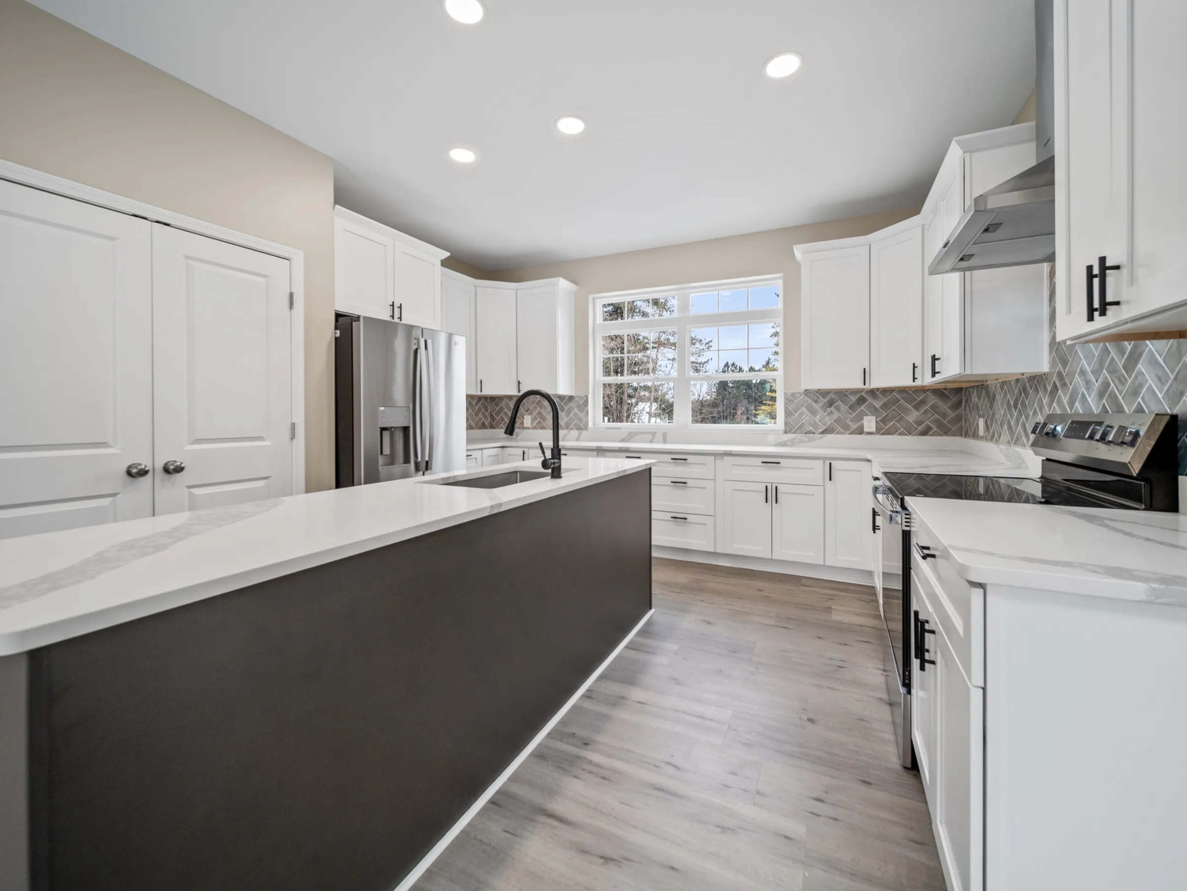 Charcoal kitchen island with a white quartz top and black hardware, against white perimeter cabinets and a herringbone backsplash.