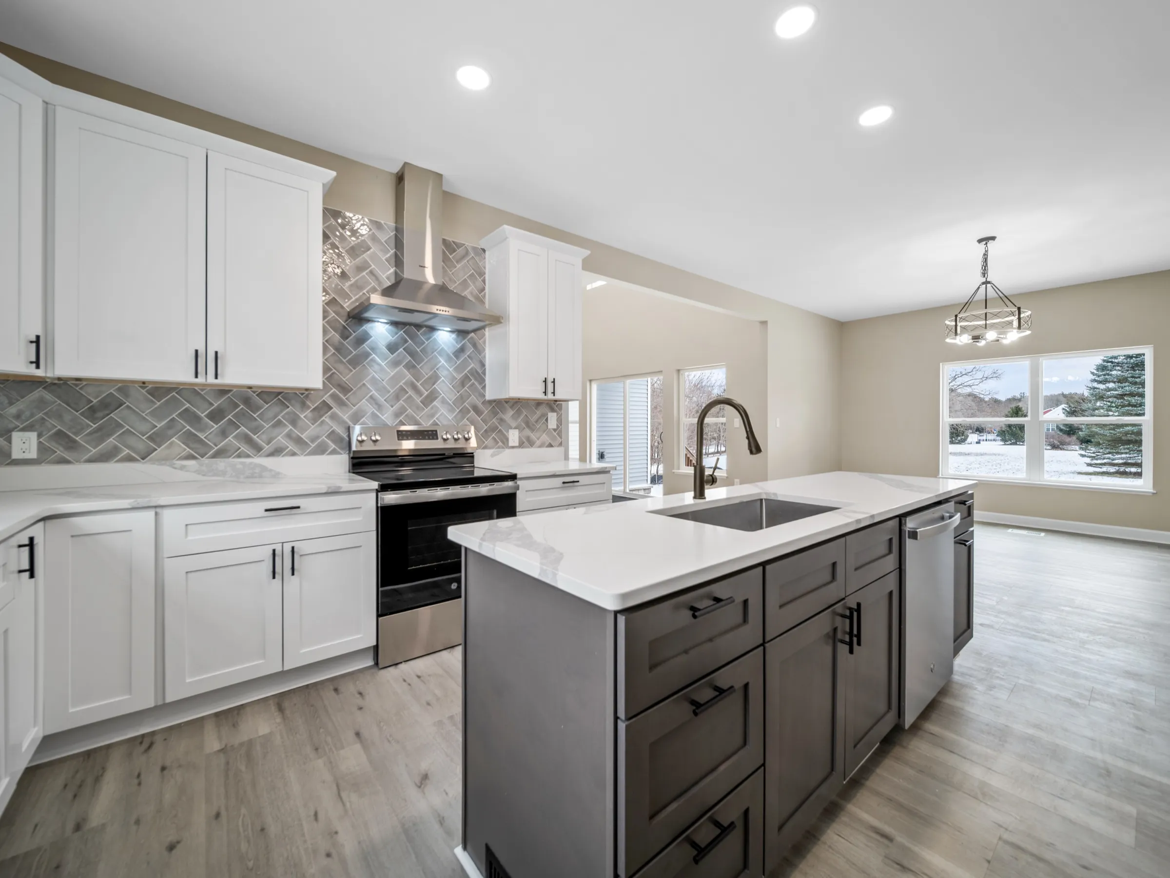 Kitchen with white shaker cabinets, a gray herringbone tile backsplash, a stainless hood over the range, and the charcoal island in front.