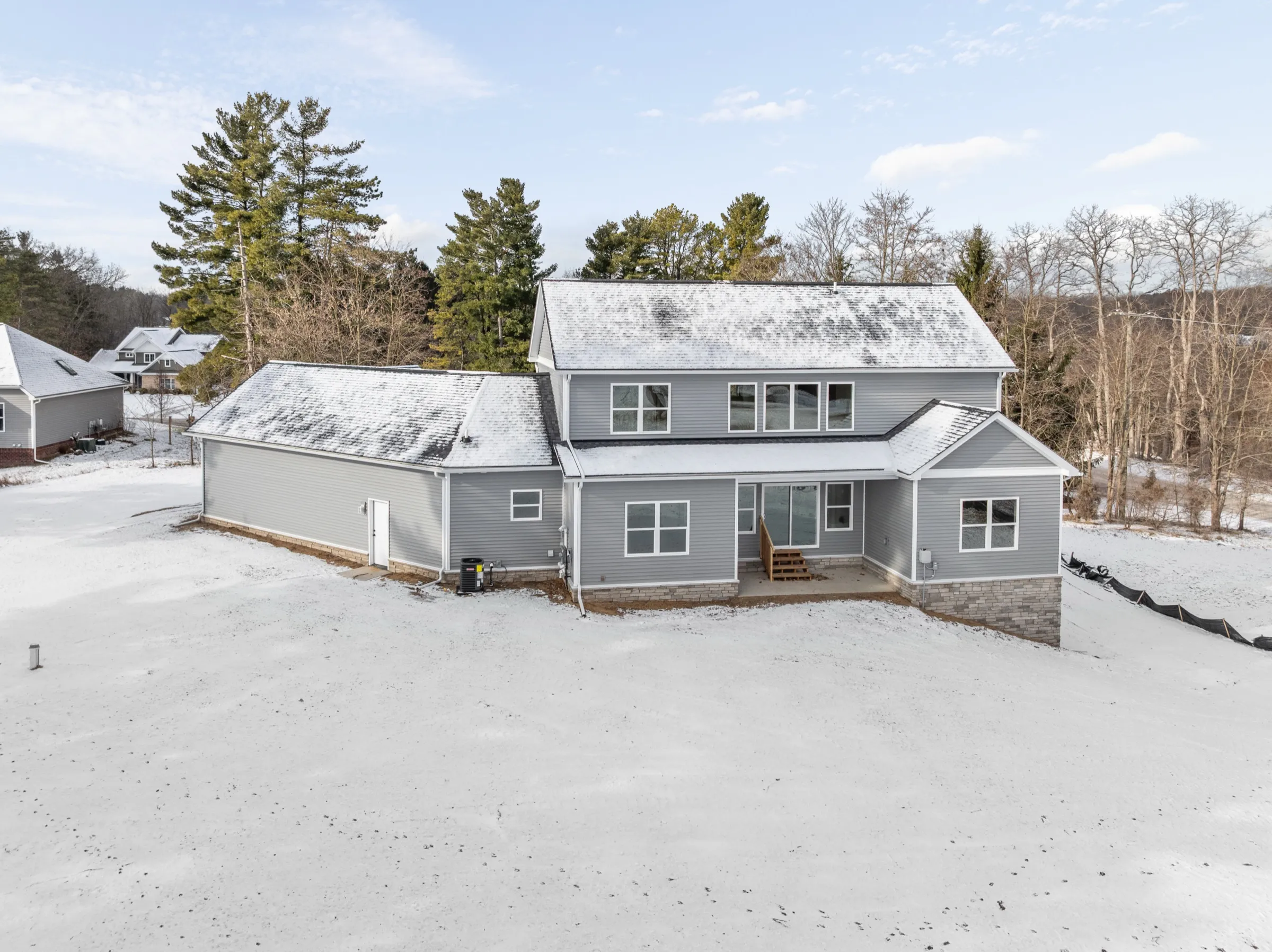 Rear elevation with a covered patio at the main floor, stone at the foundation, and the long garage wing to the left.