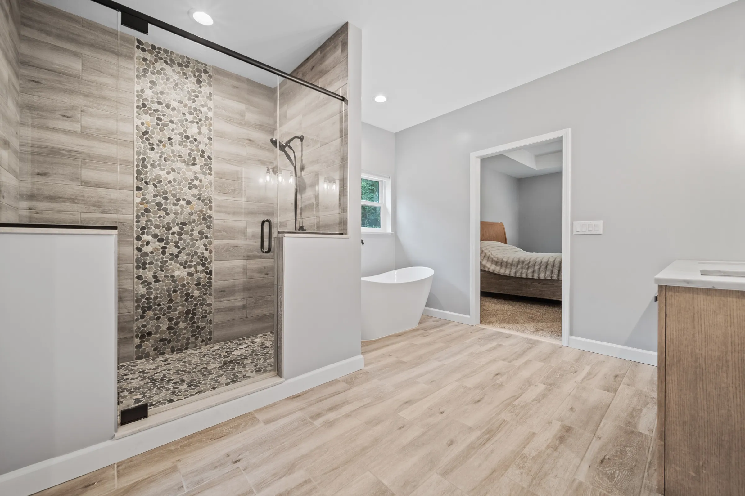Walk-in shower with a tiled feature wall and glass door, beside a freestanding soaking tub.