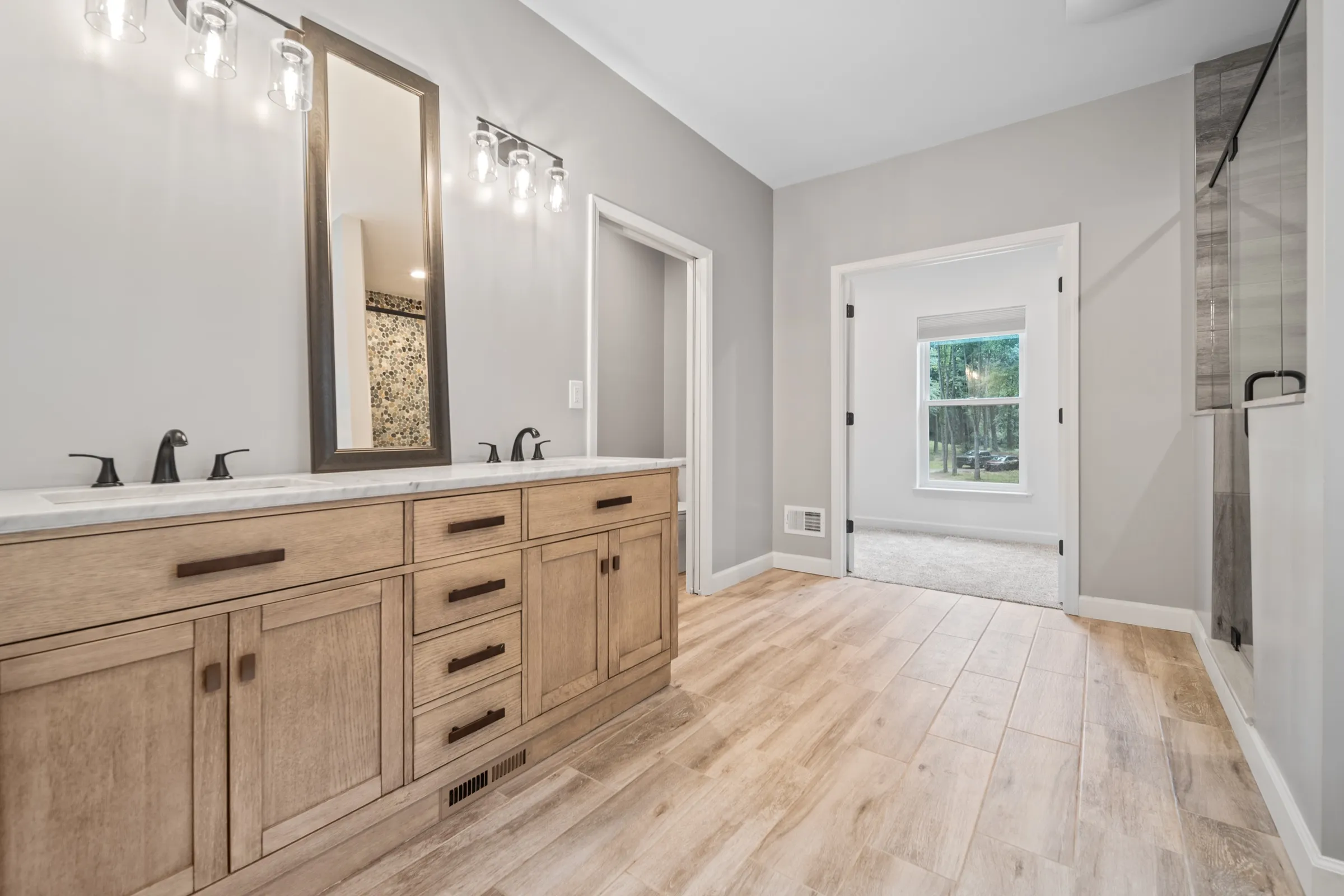 Primary bathroom with a double vanity in light oak, framed mirror and sconce lighting.