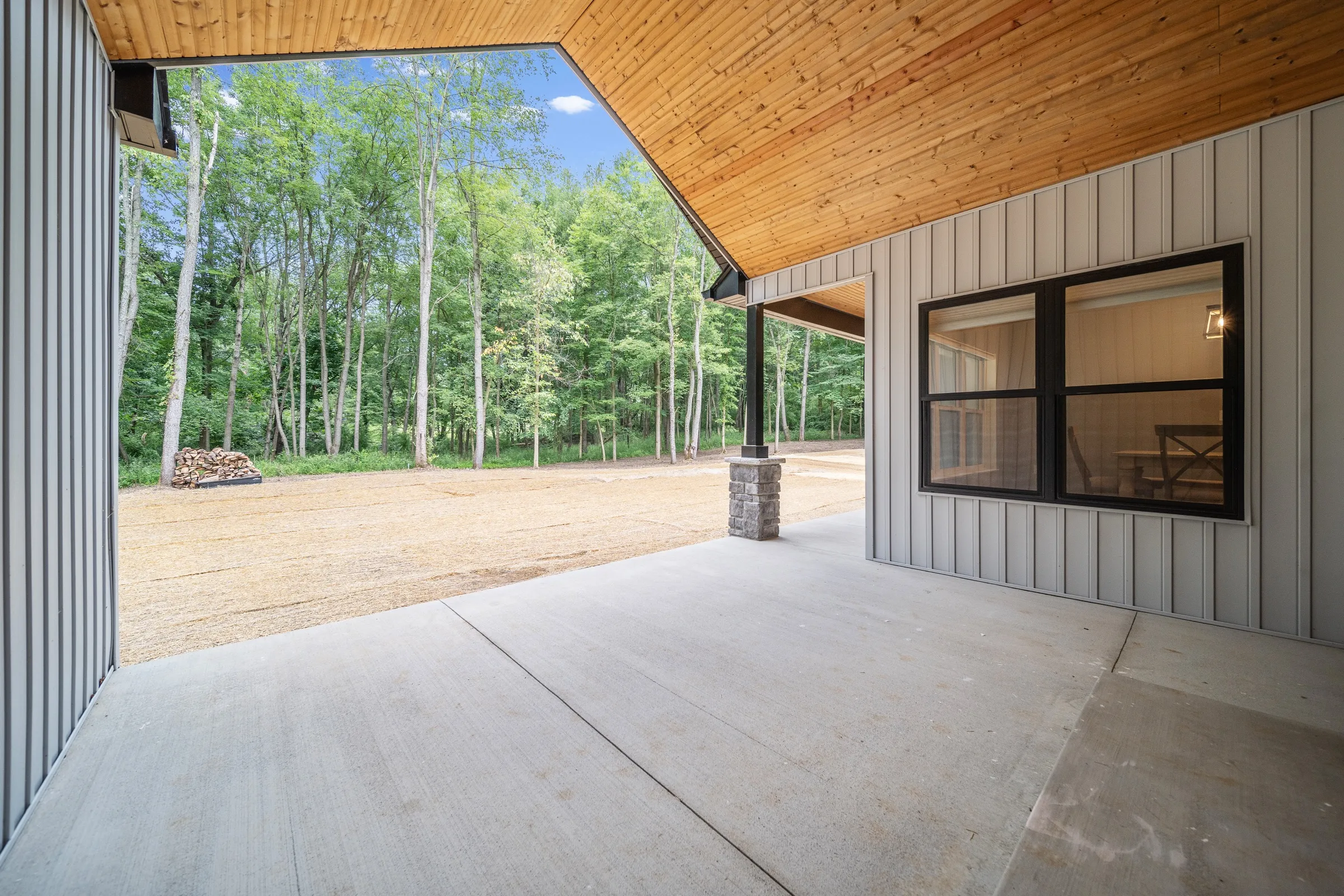 Covered concrete breezeway between house and garage, with a stained tongue-and-groove ceiling open to the woods.