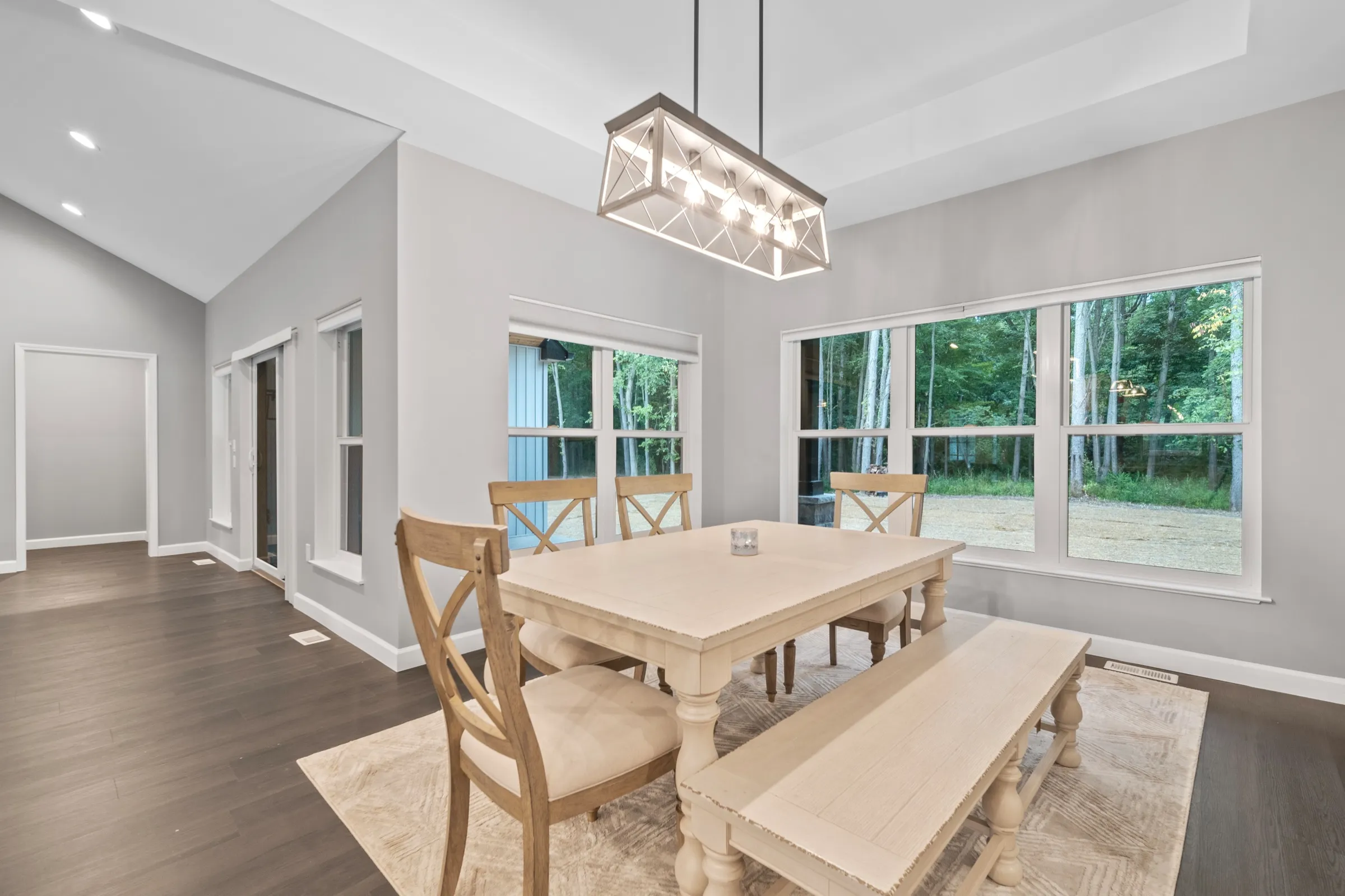Dining table and benches under a linear pendant, in front of a bank of windows looking into the woods.