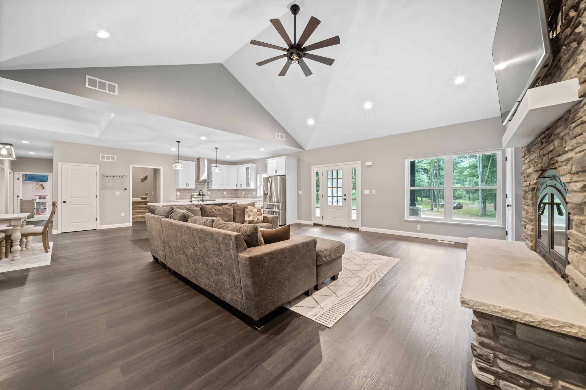 Wide view showing the great room opening into the kitchen and dining area under a single vaulted ceiling.