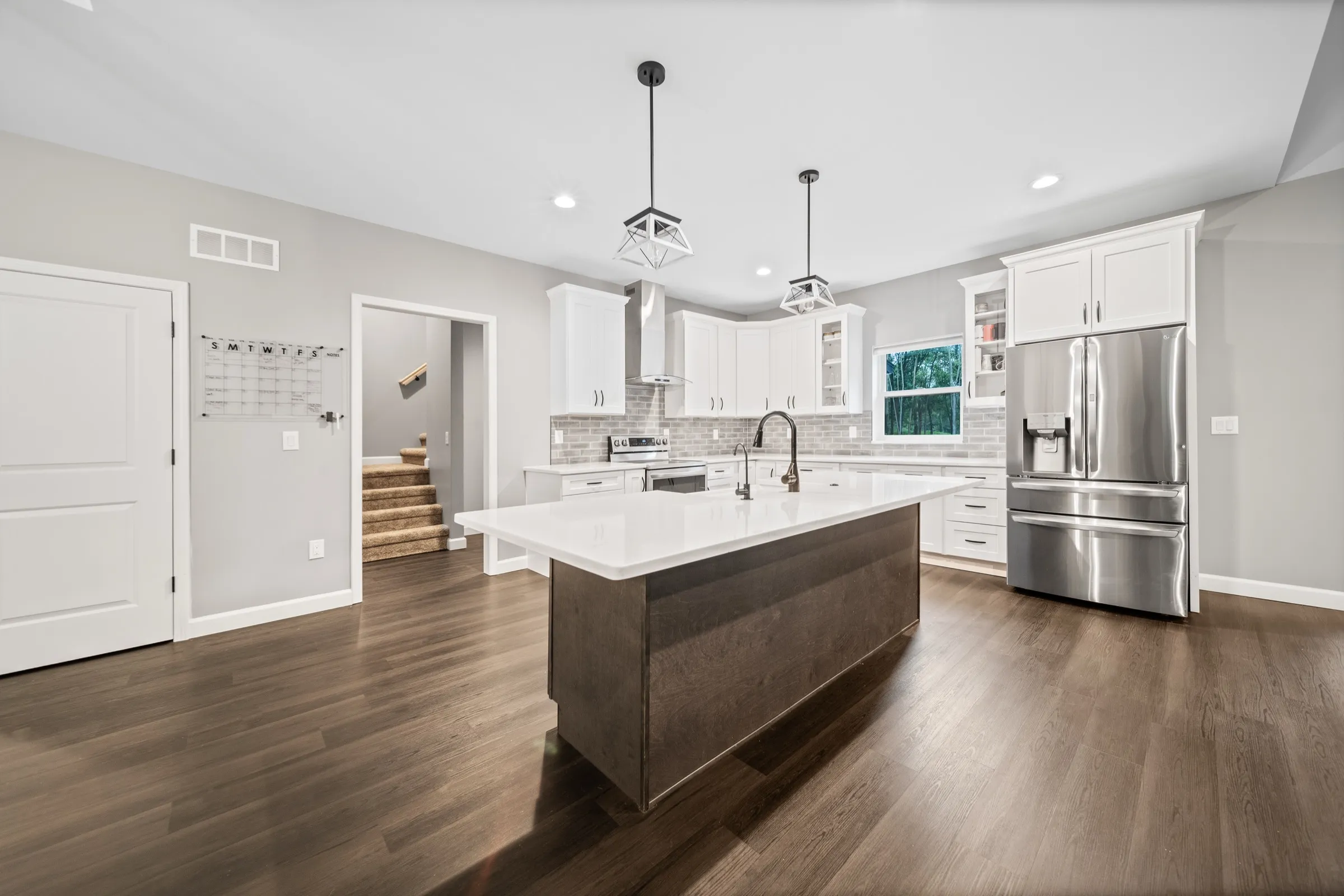 Kitchen island in stained wood with pendant lights, looking through to the back hall and stairs.