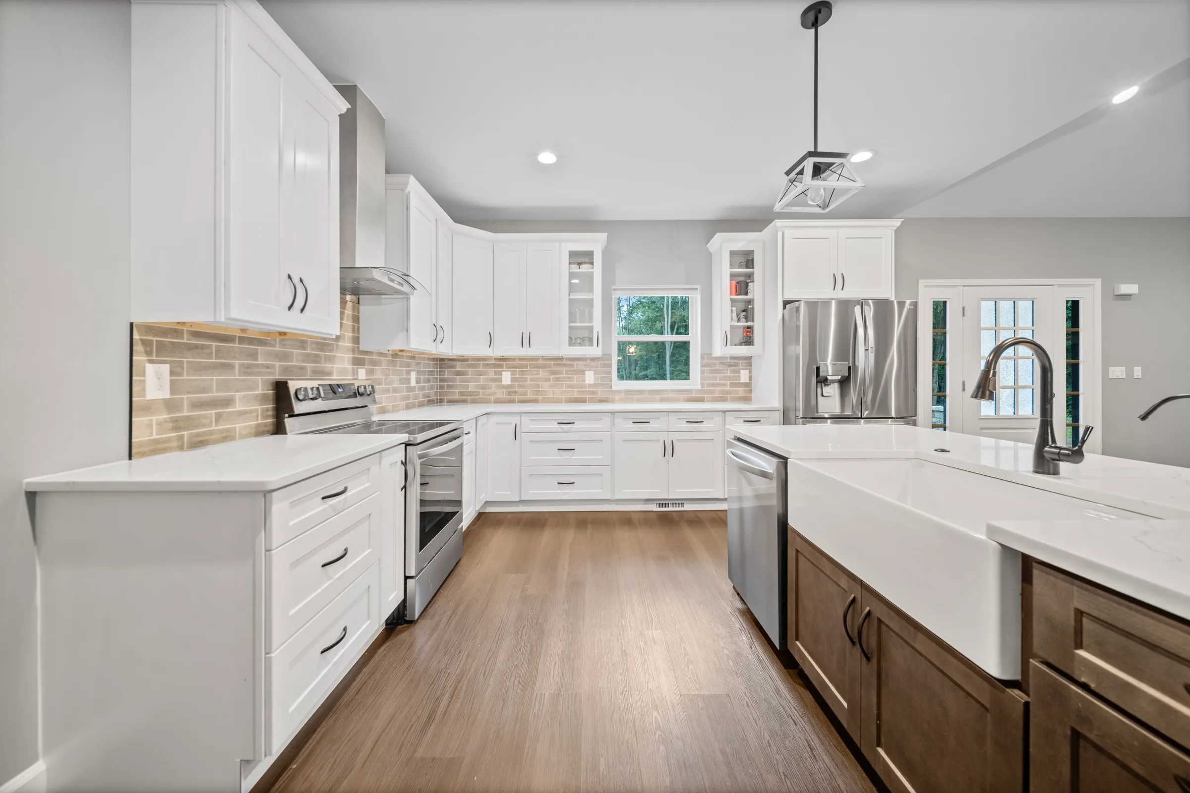 White shaker kitchen with a brick backsplash, stainless range, quartz counters and a farmhouse apron sink in a stained wood island.