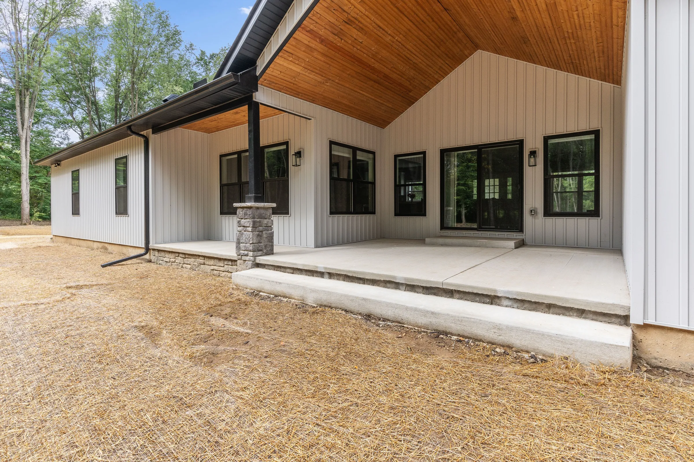 Rear elevation of the house with a long covered porch, stained wood ceiling and black-framed sliding doors.